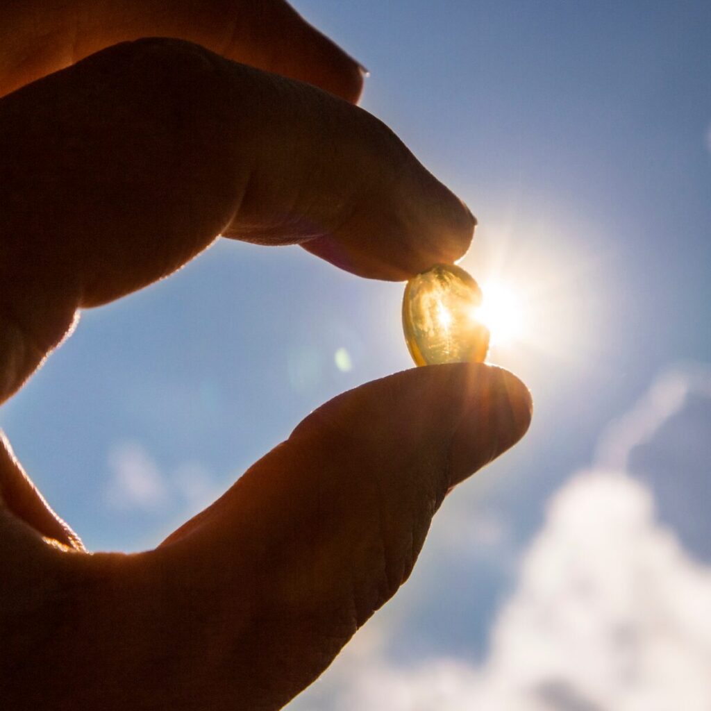 Hand holding vitamin D pill against sunlight.