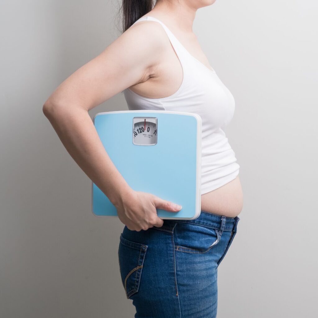 Bloated woman carrying a weighing scale.