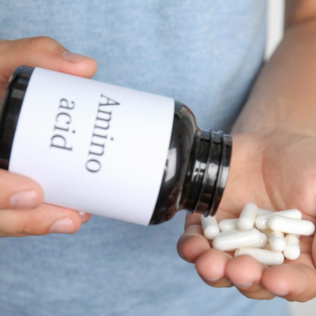 Person holding bottle of amino acid pills.