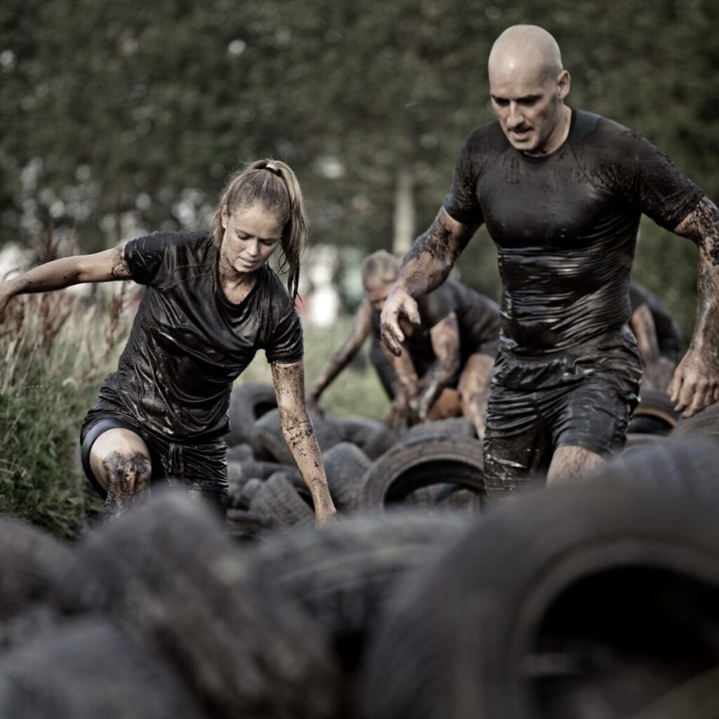 Man and woman running through mud obstacle course with tires.