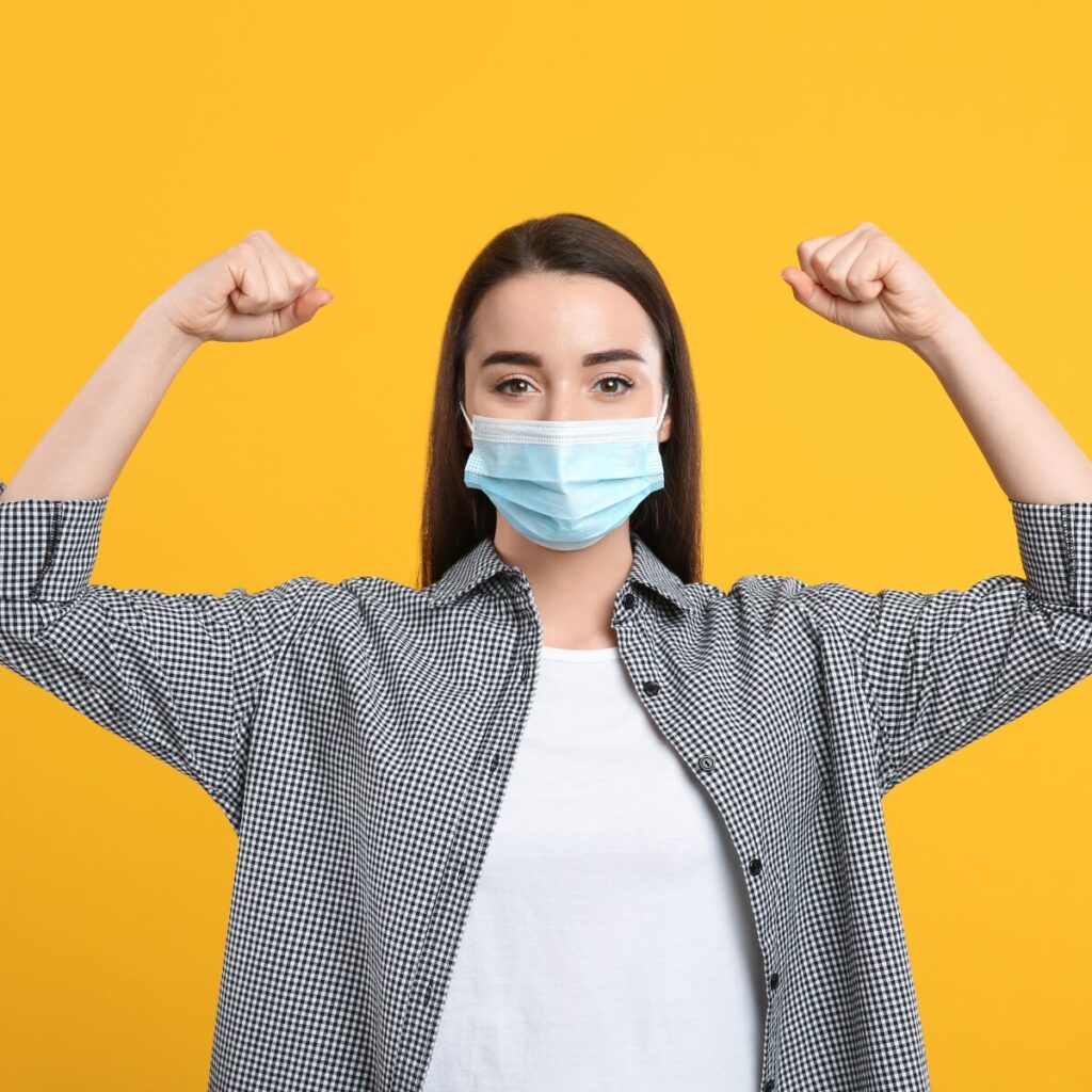 Woman wearing a mask flexing her arms.