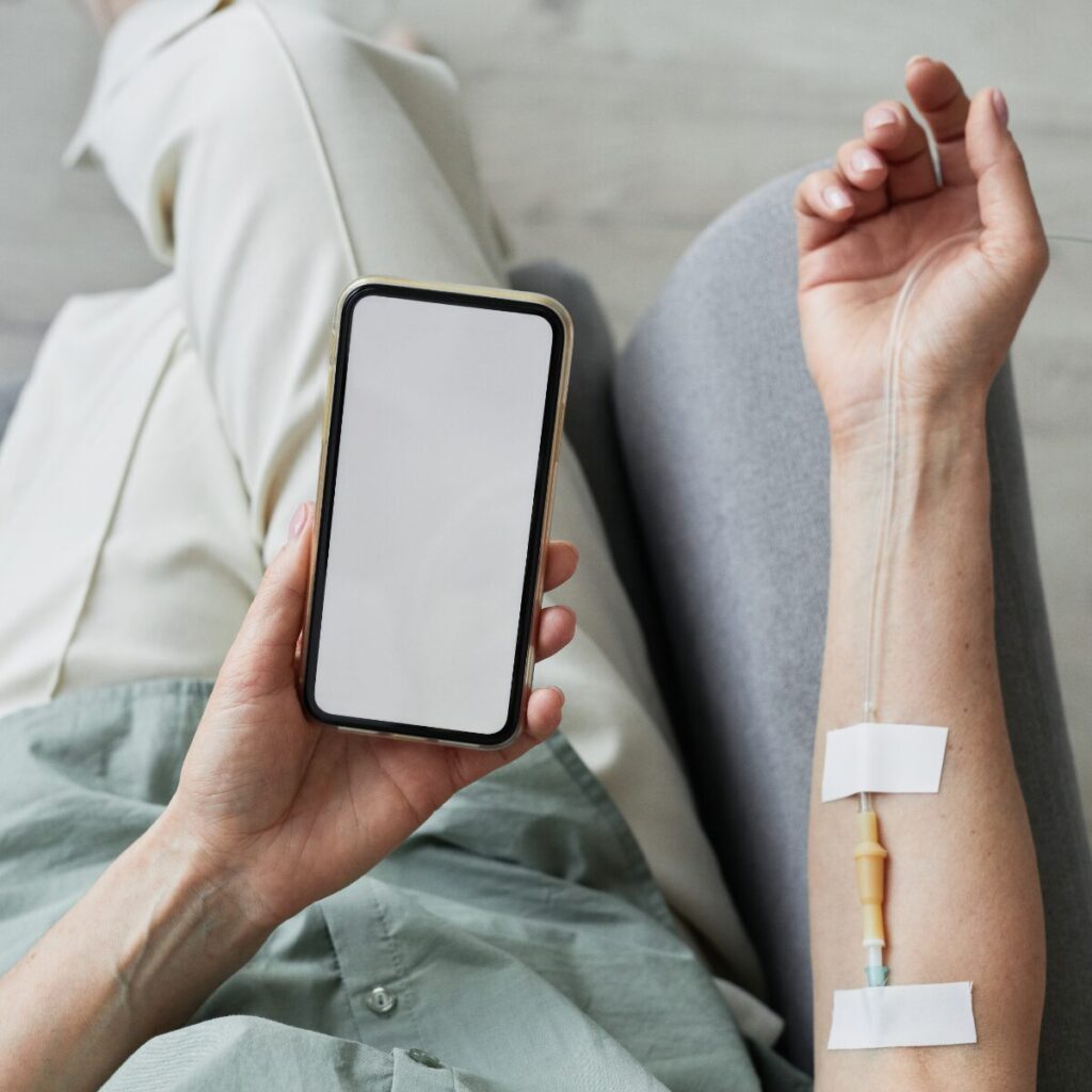 Person holding phone while getting an IV therapy.