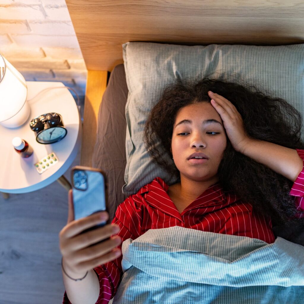 Woman holding phone in bed and having trouble sleeping.