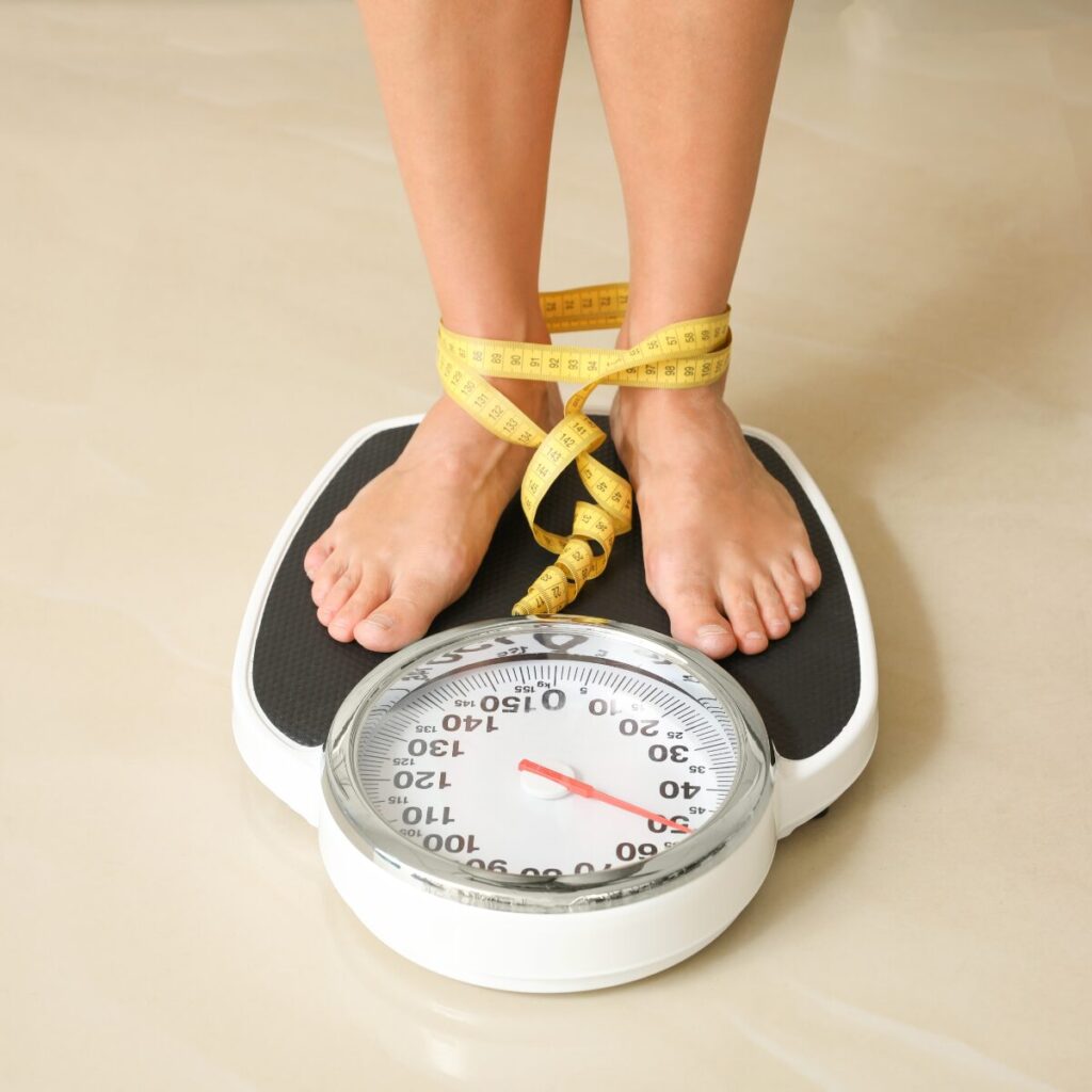 Person standing on a weighing scale with measuring tape wrapped on feet.