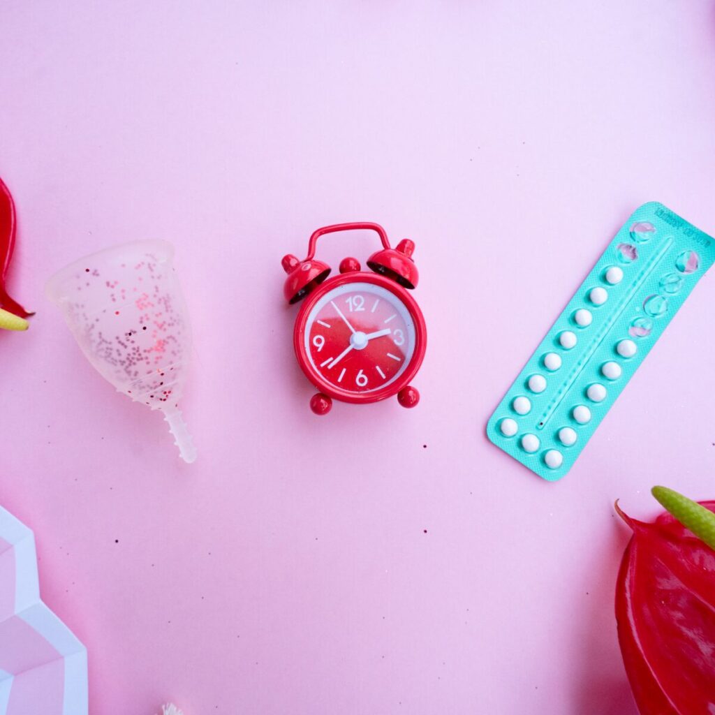 flat lay of menstrual cup, clock, and HRT pills.