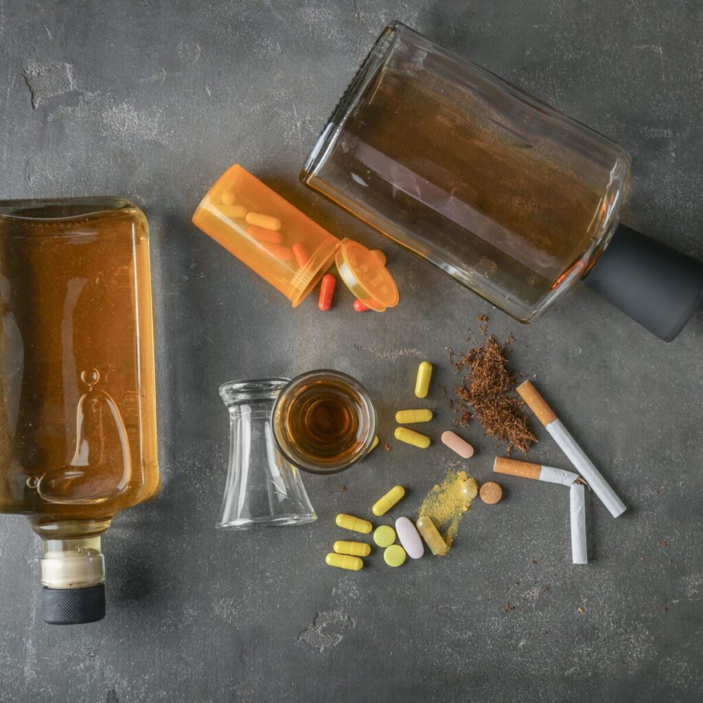 Alcohol, drugs, and cigarettes on a dark surface.